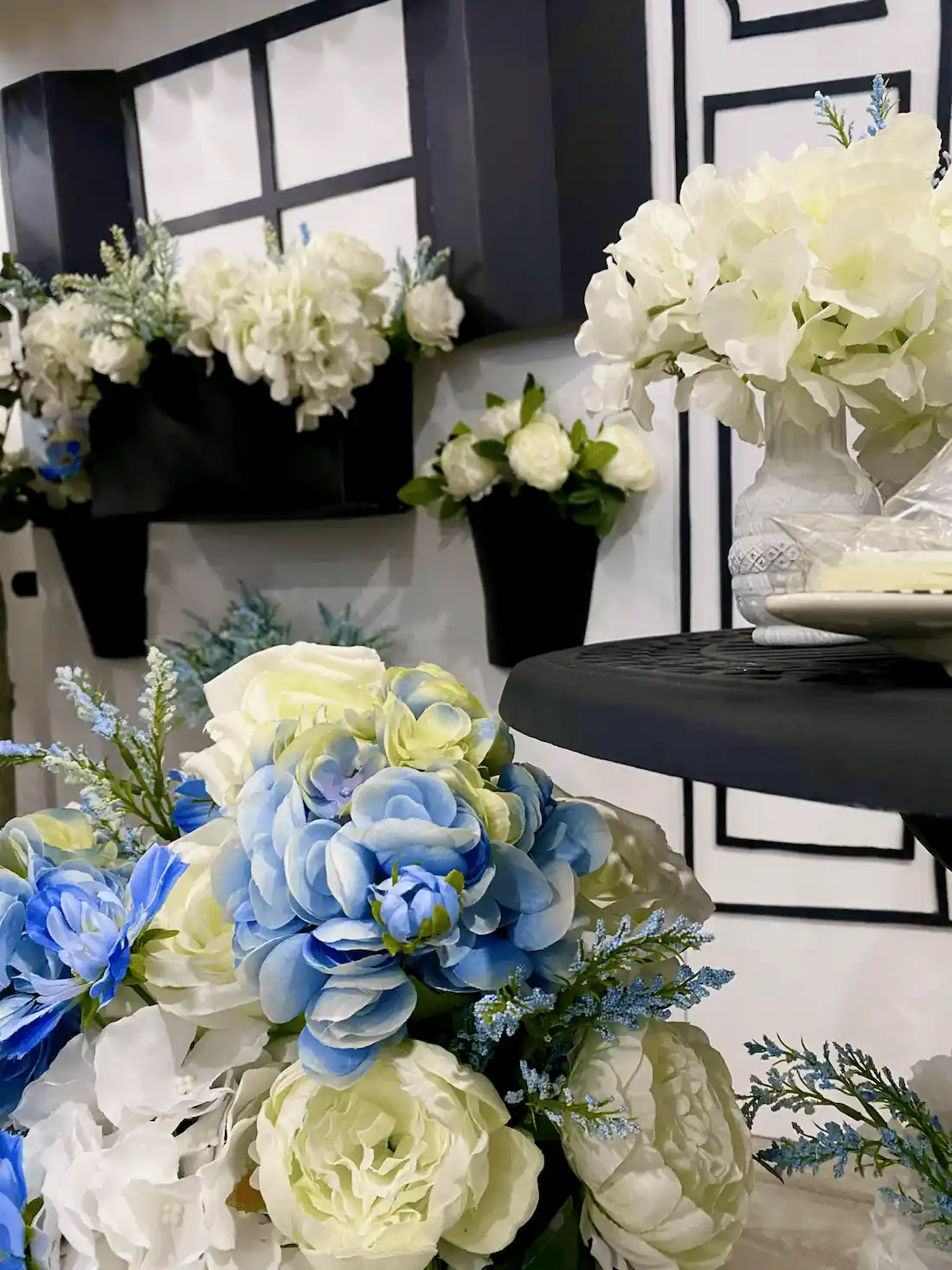 A stunning floral arrangement featuring blue and white roses, hydrangeas, and frosty greenery, elegantly displayed against a black-and-white Parisian-themed backdrop for a luxurious event setting.