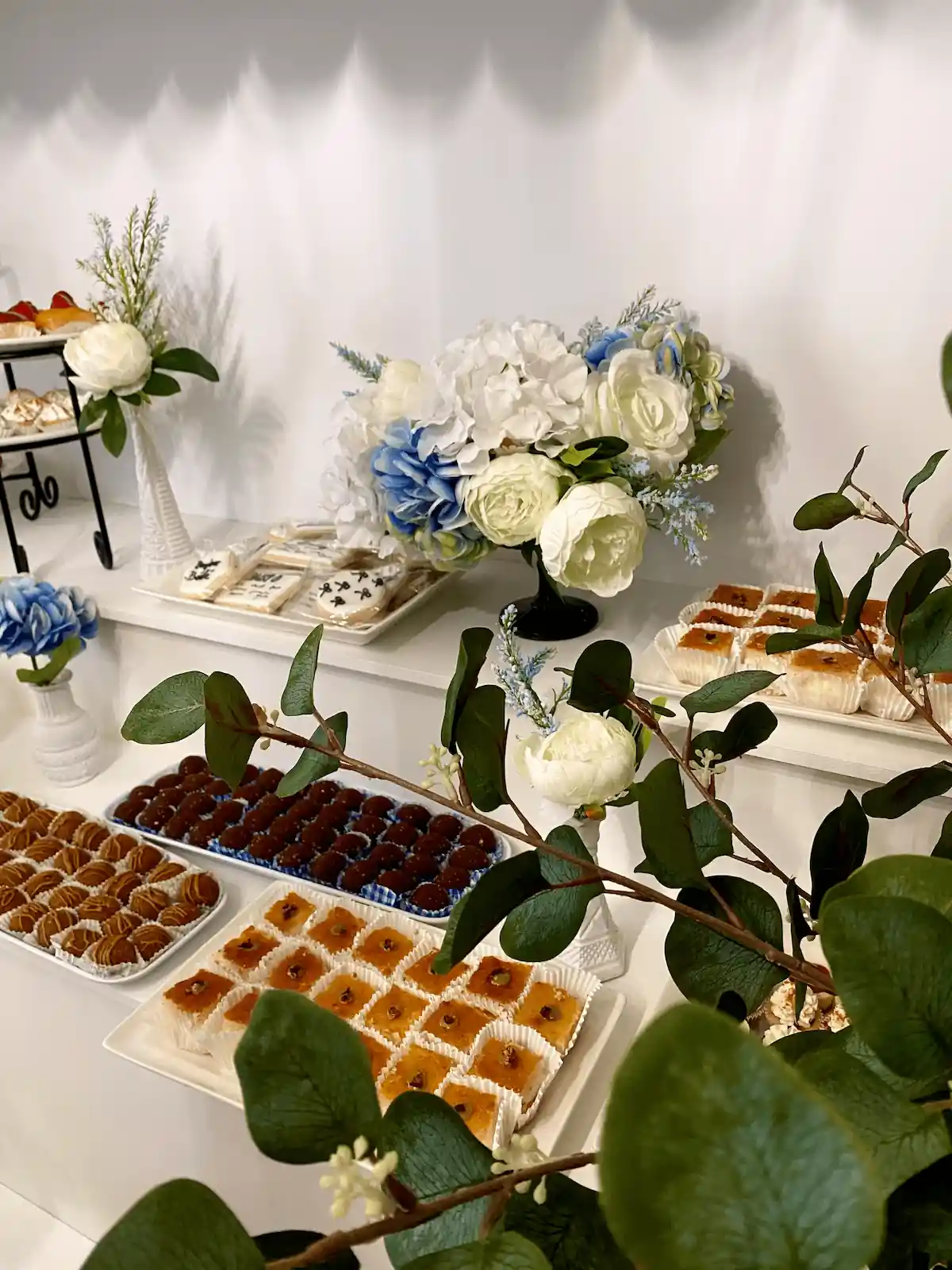 A sophisticated dessert table featuring assorted pastries, truffles, and tarts, accompanied by blue and white floral decor, creating an exquisite visual for a high-end event or baby shower.